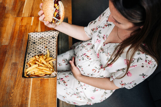 Fast food burger eat pregnant girl. Pretty young happy pregnancy woman eating tasty hamburger. Junk food concept.