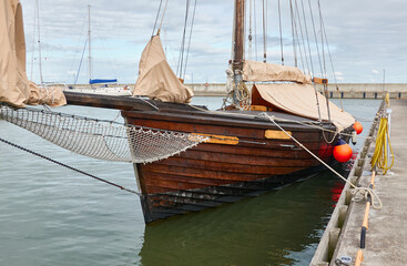 Obraz premium Vintage wooden sailboat moored to a pier in a yacht marina. Kuivastu harbour, Estonia. Transportation, summer vacations, recreation, amateur sailing and cruising, traditional craft