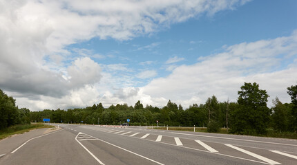 Fototapeta premium Empty highway through the forest on a sunny day. Asphalt road surface marking. Estonia, Europe. Transportation, traffic law, wanderlust, remote places, summer vacations concepts