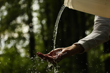 Young man hand and water pouring from a canister on a green background. Pavel Kubarkov, my right hand and water. Photo was taken 17 August 2022 year, MSK time in Russia. - 527568251