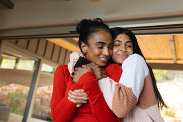 Happy biracial teenage daughter with eyes closed hugging mother from behind at home