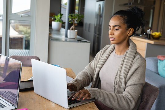 Biracial mid adult woman working over laptop on wooden table at home, copy space
