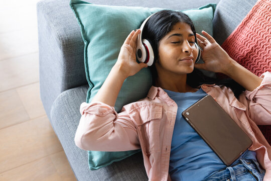 High angle view of biracial teenage girl with eyes closed listening music while lying on sofa