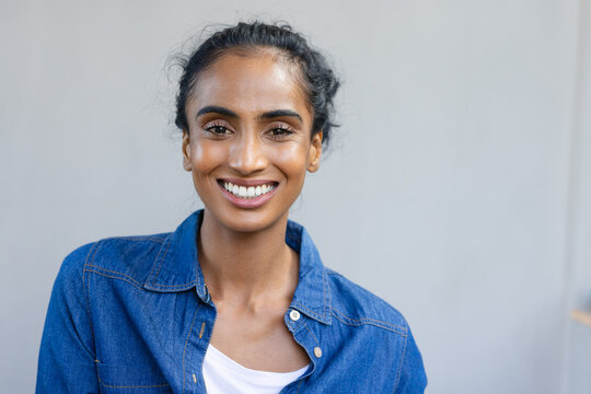 Portrait of smiling biracial mid adult woman wearing denim shirt against white wall at home