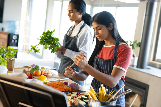 Biracial mother and daughter wearing aprons and preparing food in kitchen, copy space