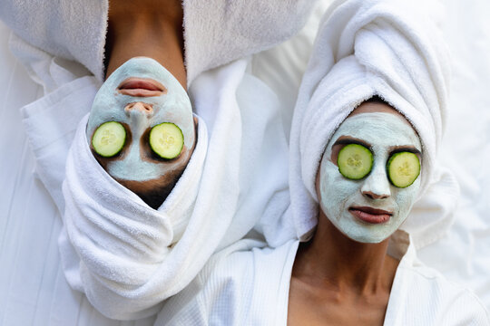 Biracial mother and daughter with facial masks and cucumber slices on eyes lying at home
