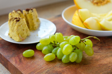 a plate of melon slices, homemade cake, green grapes on a wooden background, concept of fresh fruits and healthy food
