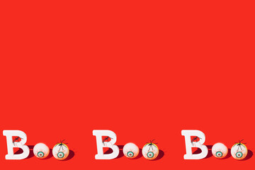 Boo scary concept. Halloween background with creative text spiders and bloodshot eyes against vibrant red. Copy space.