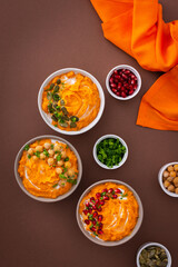 Pumpkin puree soup of butternut squash in bowls with chickpeas and green onions, pumpkin and pomegranate seeds, top view on plates with food on brown background