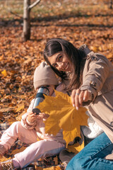 Happy dark-haired young mother and daughter having fun at a picnic in the autumn park on a sunny day.Family and autumn concept.