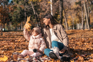 Happy dark-haired young mother and daughter having fun at a picnic in the autumn park on a sunny...