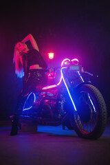 Plakat Young beautiful girl in the neon lights stands near the motorbike.