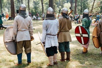 Vikings in helmets with weapons standing on the battlefield outdoors, rear view. Reconstruction of...