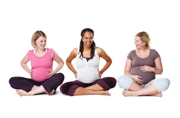 Obraz na płótnie Canvas Pregnant friends sitting against a studio white background, enjoying getting healthy and prenatal care together. Diverse mothers in a birth class, bonding and learning relax and stress relief tips