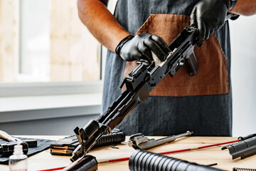 Close up of a man in apron wiping his firearm with a cloth - obrazy, fototapety, plakaty