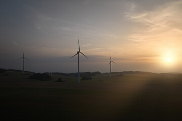 Obraz premium Aerial, scenic view of wind power plant silhouette against sunset. Aerial, drone inspection of three wind-powered electrical generators.