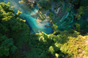 Clear, blue-green water of a mountain spring of Bistricë river in oak and sycamore forest, scenic view of genuine pure nature, aerial, perpendicular view. Traveling through Albania.