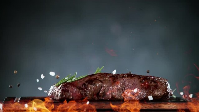 Flying pieces of grilled beef steak and spices falling on table with fire. Filmed on high speed cinema camera, 1000 fps. Speed ramp effect.