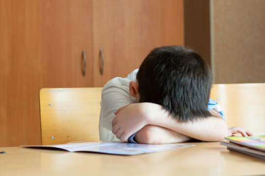 Tired boy student sits with his head on the table at school