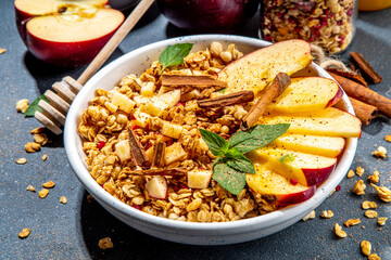 Healthy autumn breakfast granola. Apple pie granola with muesli, cinnamon spices, apples slices, honey and nuts, on black stone background copy space