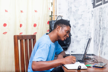 Serene young black African male student home studying online with laptop and writing on a journal