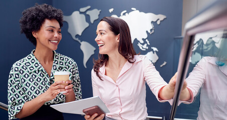 Two Female Colleagues Have Informal Meeting On Stairs Of Modern Office With World Map In Background