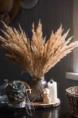 Candles, succulent, basket and a beautiful bouquet of dried pampas grass flowers in a glass vase on...