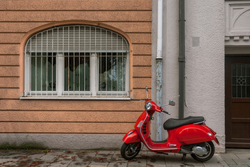 Red scooter parked by the wall in an empty street in Munich Germany. 