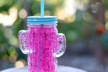Cactus shaped glass filled with pink soda in the garden. Refreshing summer drink. Selective focus.