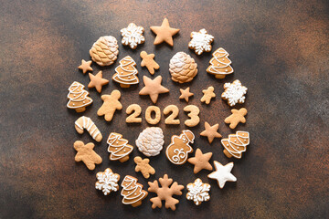 Obraz na płótnie Canvas Christmas assorted glazed cookies with date 2023 inside on brown background. New Year greeting card. Top view. Xmas festive holiday.