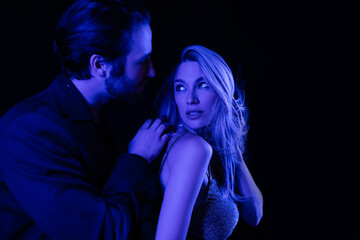 Young man touching seductive blonde girlfriend with blue lighting isolated on black.