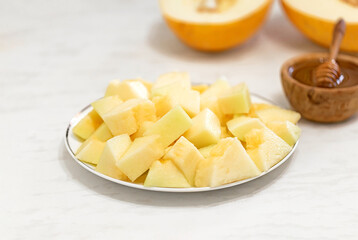 Slices of ripe melon with honey on a plate on a white table. Healthy eating at home. Selective focus