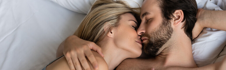 top view of couple in love kissing with closed eyes on bed, banner.
