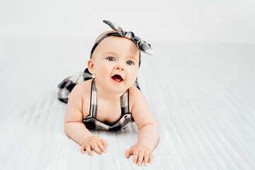 Seven month old baby child sitting on bed. Cute smiling little infant girl on white soft blanket. girl wearing headband. Charming blue eyed baby. Copy space.