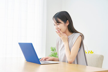 リビングでノートパソコンを見て笑顔で驚く女性
