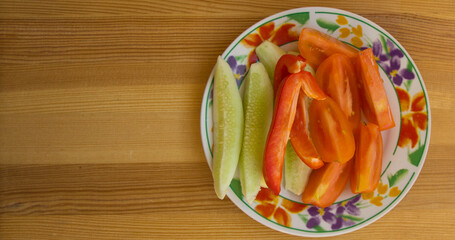 Sliced ​​vegetables for salad tomatoes, lettuce, peppers on a plate with a pattern on a wooden table