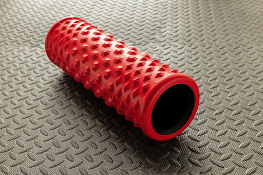 Red foam roller for deep tissue and muscle massage and myofascial trigger point release  on black mat 