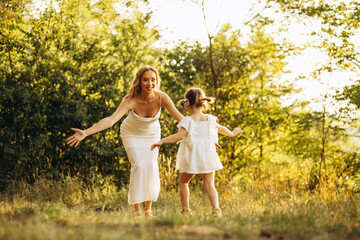Mother with little daughter in beautiful dresses walking in forest