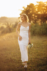 Fototapeta na wymiar Woman bride in simple white dress with bouquet of flowers walking in the field