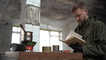 Stalker sits at the table inside of abandoned building and reading book. Cyberpunk post apocalypse or air pollution. Post-war days.