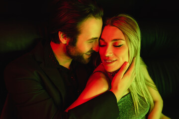 Positive man touching sexy blonde girlfriend with lighting isolated on black.