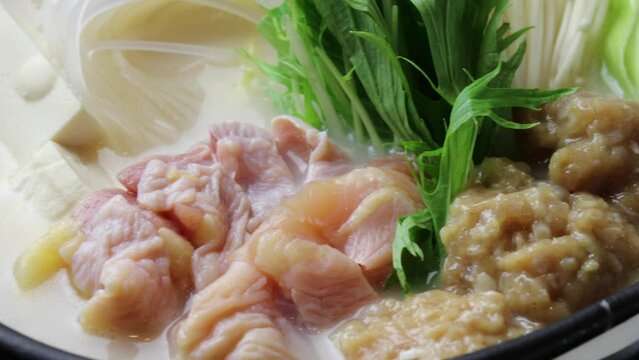 鶏もも肉、鶏つくね、水菜、豆腐を白濁した鶏白湯スープで煮込む鍋料理。土鍋で加熱される具材を捉えた接写・クローズアップ映像。飲食店メニュー、レシピ解説、冬の料理、和食の広告や映像素材に。 | Close-up of chicken and vegetable hot pot in creamy white soup.
