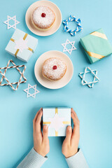 Jewish holiday Hanukkah concept - Hanukkah sweet doughnut with powdered sugar and fruit jam, gift boxes on blue paper background.