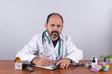 Portrait of senior mature doctor, pleasant professional in white coat sitting at table