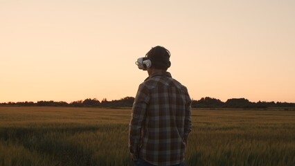 Farmer in virtual reality helmet in front of a sunset agricultural landscape. Man in a countryside field. Country life, food production, farming and technology concept