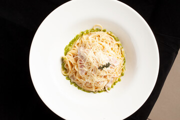 Pasta with bacon and cheese in a plate. On a dark background.