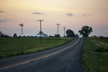 Fototapeta premium Sunset over rural farm with power lines and windmill