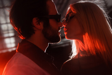 Side view of stylish couple in sunglasses kissing in lighting during party.