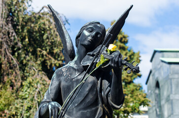La statua bronzea di un angelo che suona il violino su cui hanno appoggiato una rosa gialla su una...