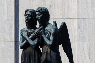 La statua bronzea di un angelo che conforta una donna in preghiera su una tomba dell cimitero...